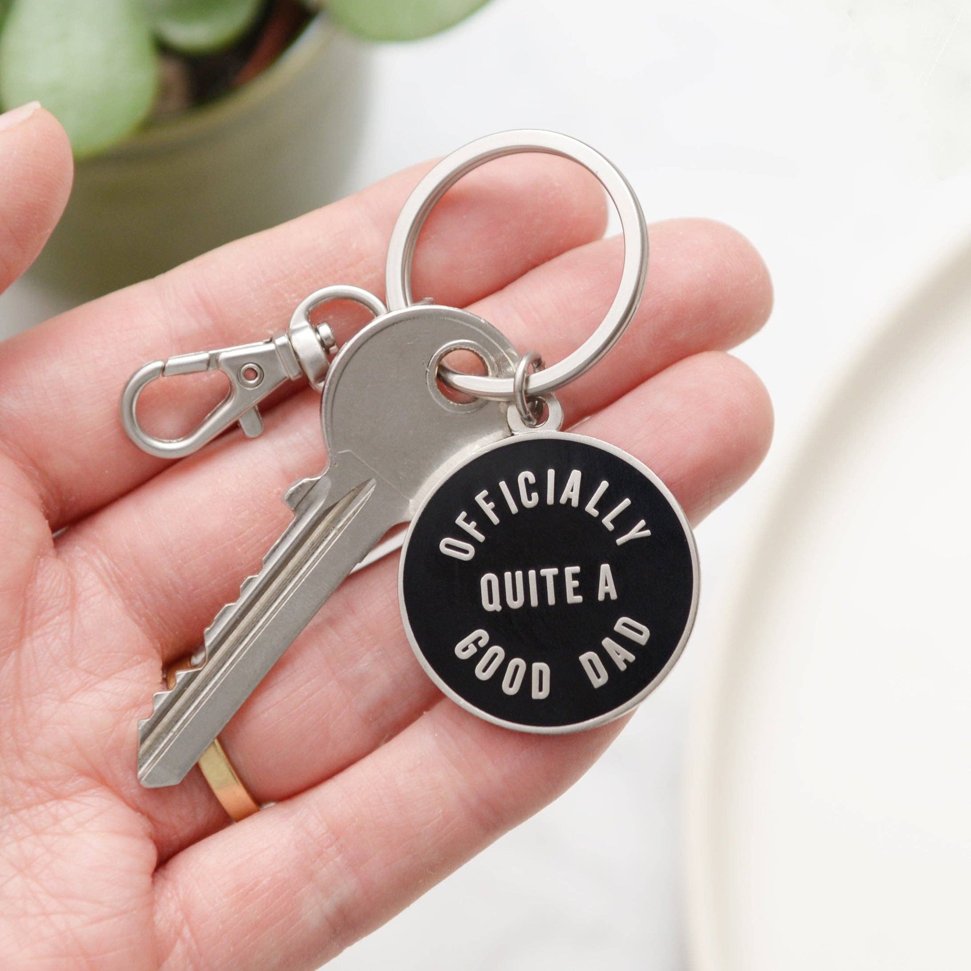 Keychain with a tag reading 'Officially Quite a Good Dad' held in a hand.