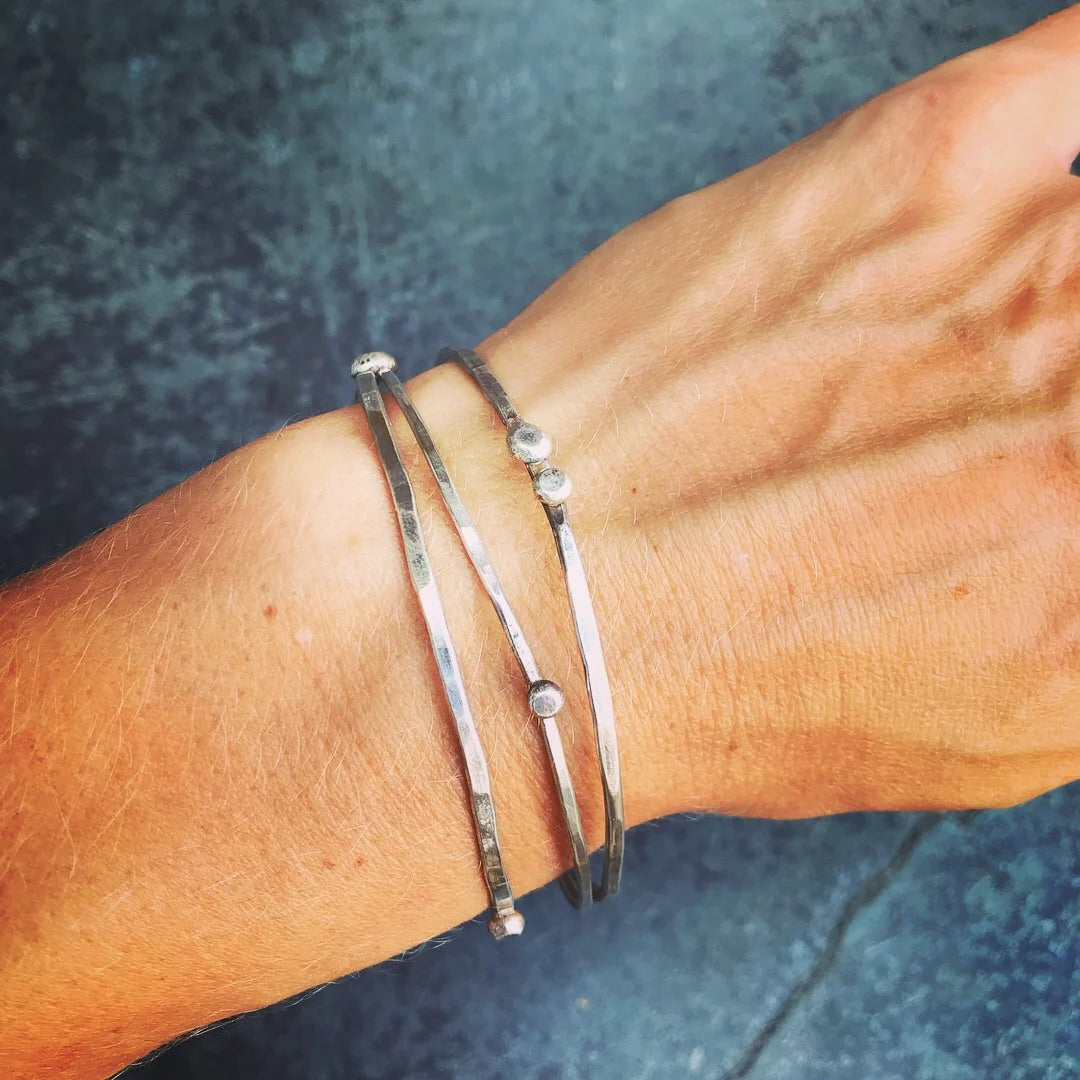 Silver bracelets on a wrist against a dark blue background