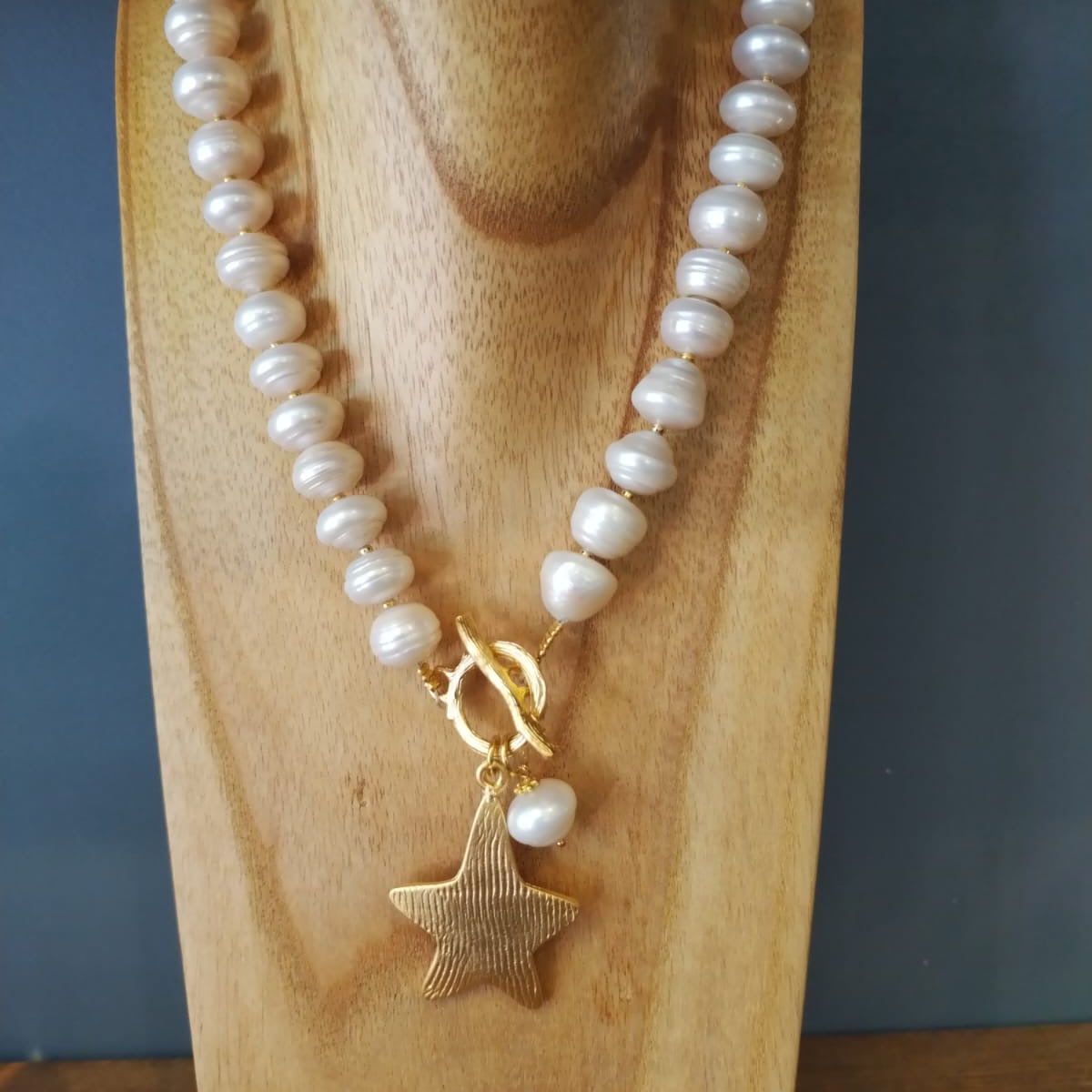 Pearl necklace with a gold star pendant on a wooden stand against a dark background