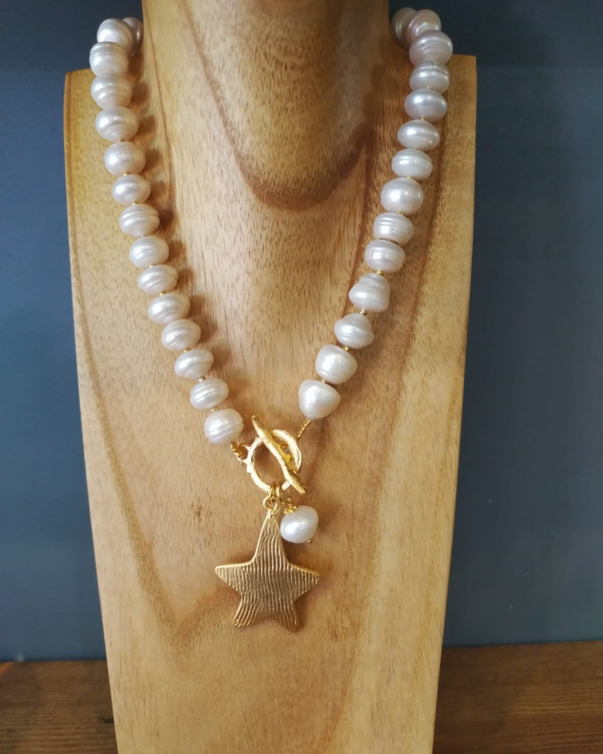 Pearl necklace with a gold star pendant on a wooden stand against a dark background