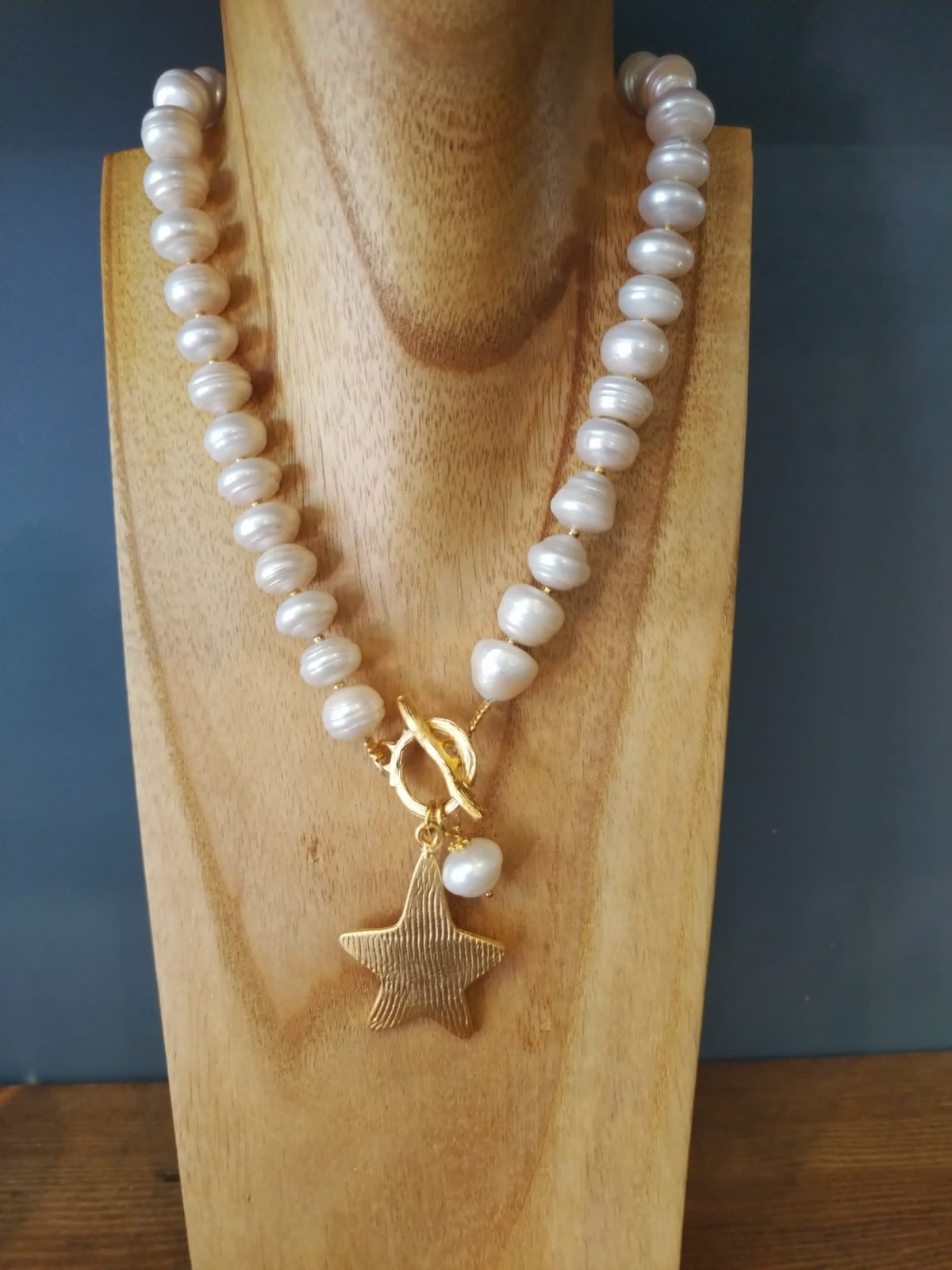 Pearl necklace with a gold star pendant on a wooden stand against a dark background
