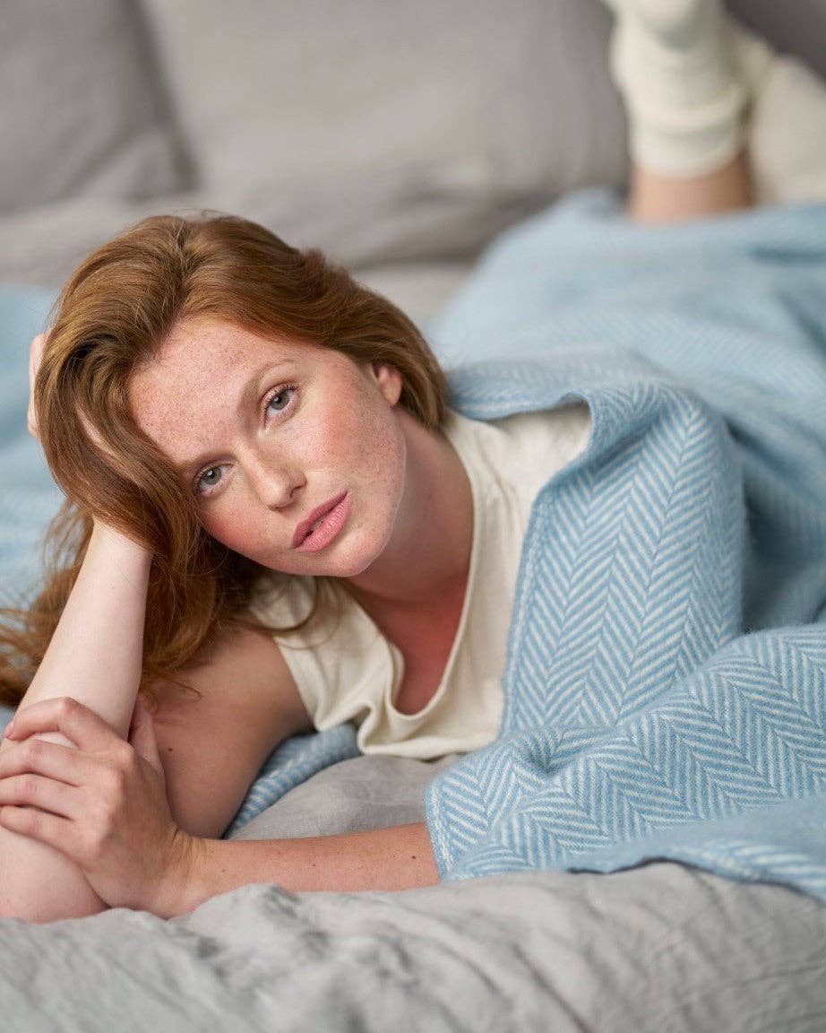 Woman lying on a bed with a blue blanket, looking at the camera.