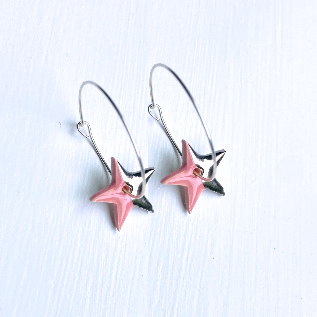 Pink and silver star-shaped earrings on a light blue background