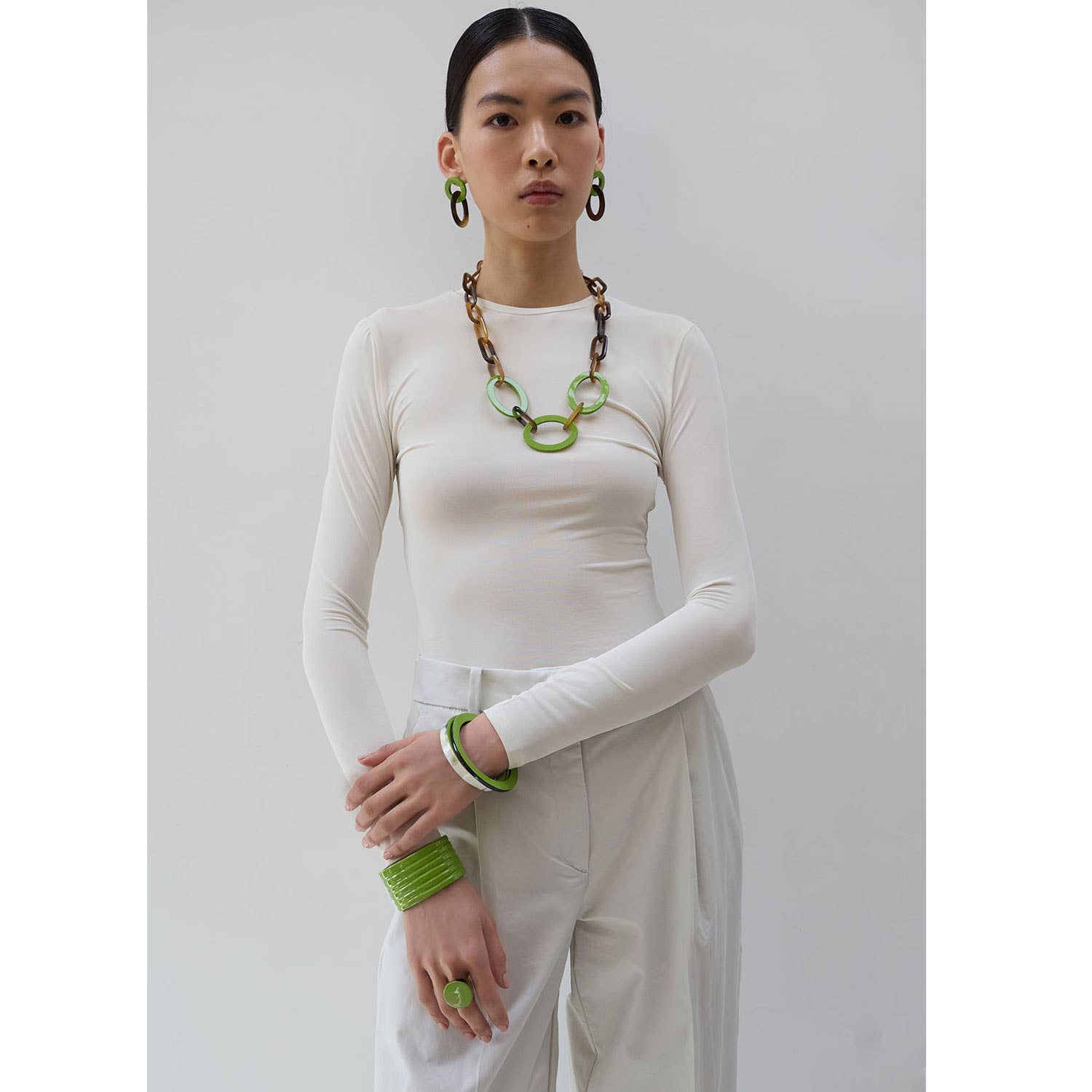Person wearing a white outfit with green accessories against a gray background