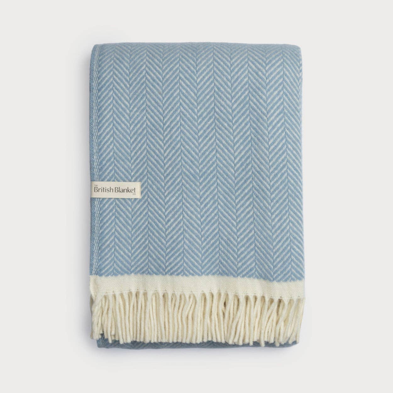 Blue and white herringbone patterned blanket with cream fringe on a light gray background
