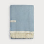 Blue and white herringbone patterned blanket with cream fringe on a light gray background
