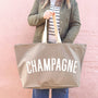 Person holding a beige tote bag with 'CHAMPAGNE' text against a pink background