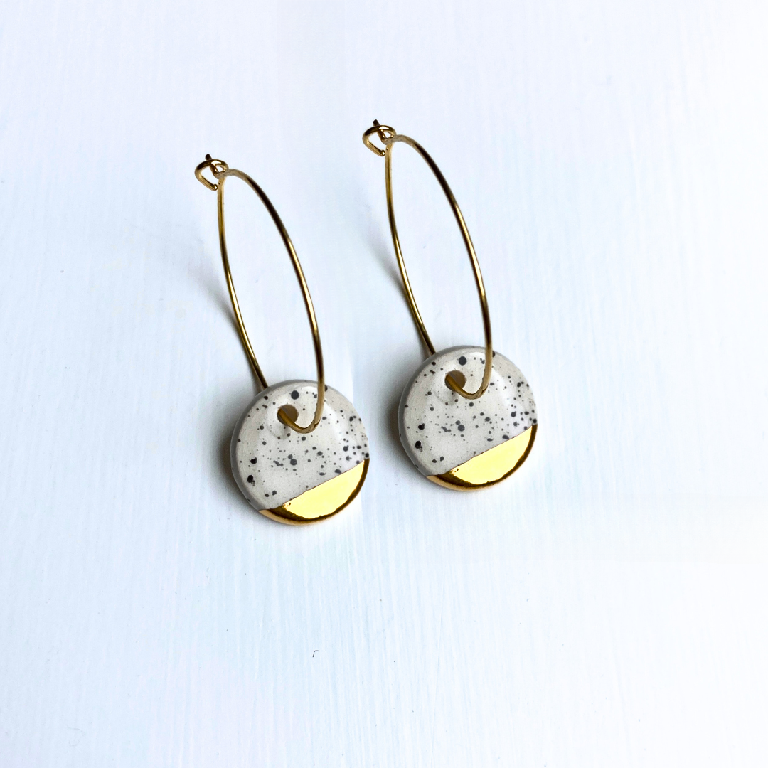 Pair of earrings with gold and white circular designs on a light blue background