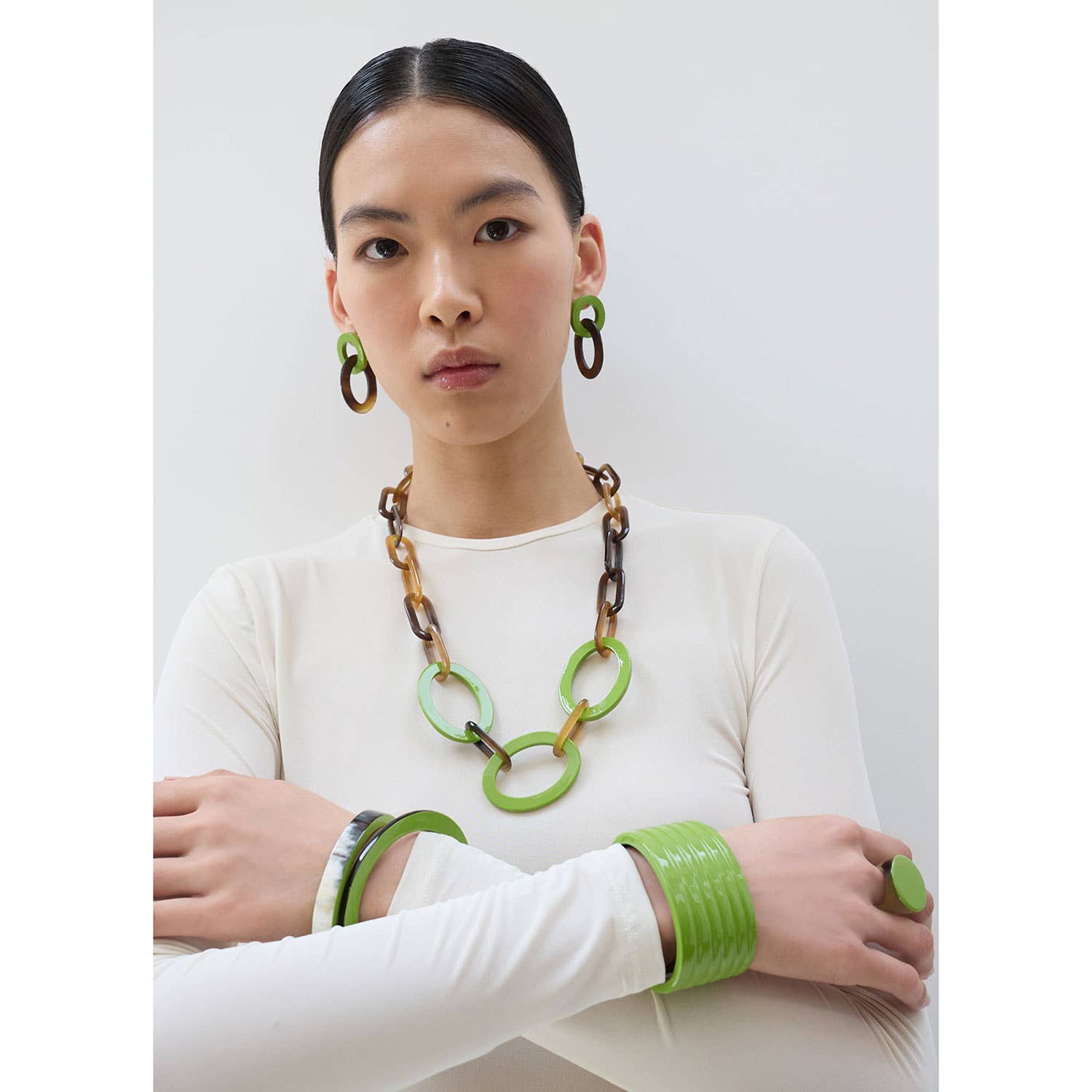 Woman wearing a white top with green and brown jewelry on a plain background