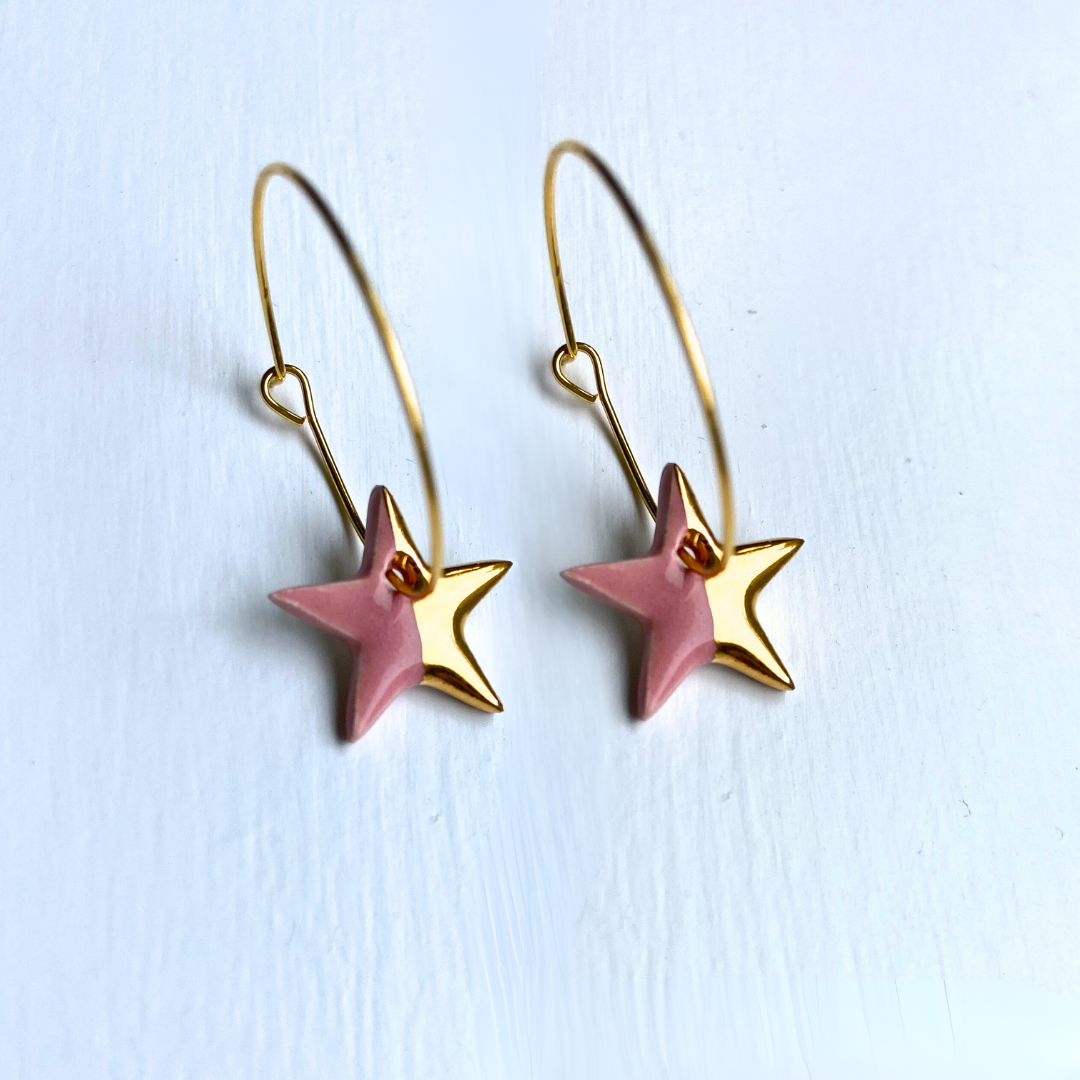 Star-shaped earrings with gold and pink details on a light blue background