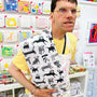 Person wearing a white apron with black dog patterns in front of a display of colorful greeting cards.