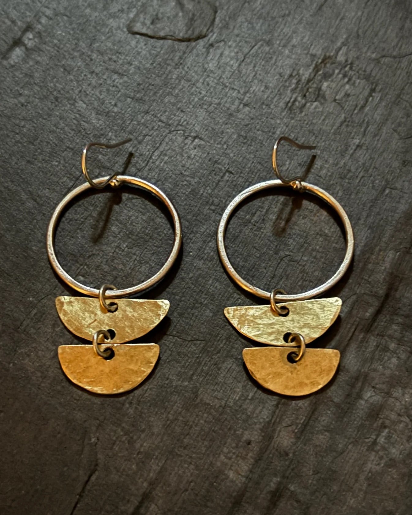 Pair of gold hoop earrings with half-circle pendants on a dark textured surface