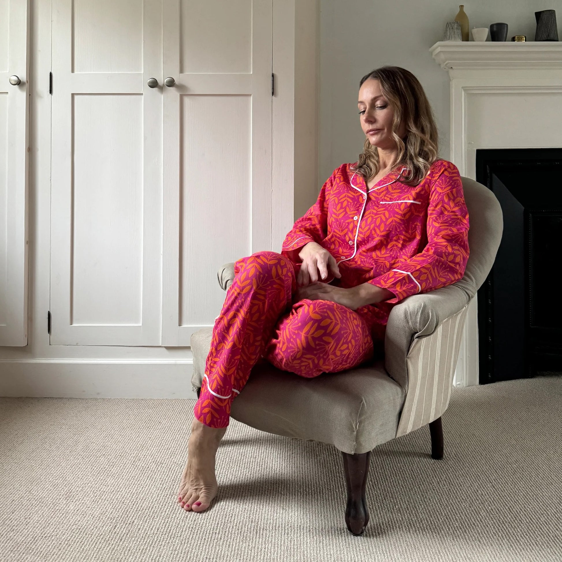 Woman in pink patterned pajamas sitting on a chair in a cozy room.