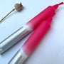 Two pink and silver markers on a white background with a dried flower.
