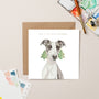 Christmas card with a dog illustration and festive trees, placed on a beige surface with art supplies.