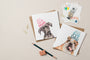 Two greeting cards with dog illustrations and text on a beige surface with stationery items.
