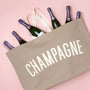 Beige tote bag with 'CHAMPAGNE' text and six bottles of champagne on a pink background