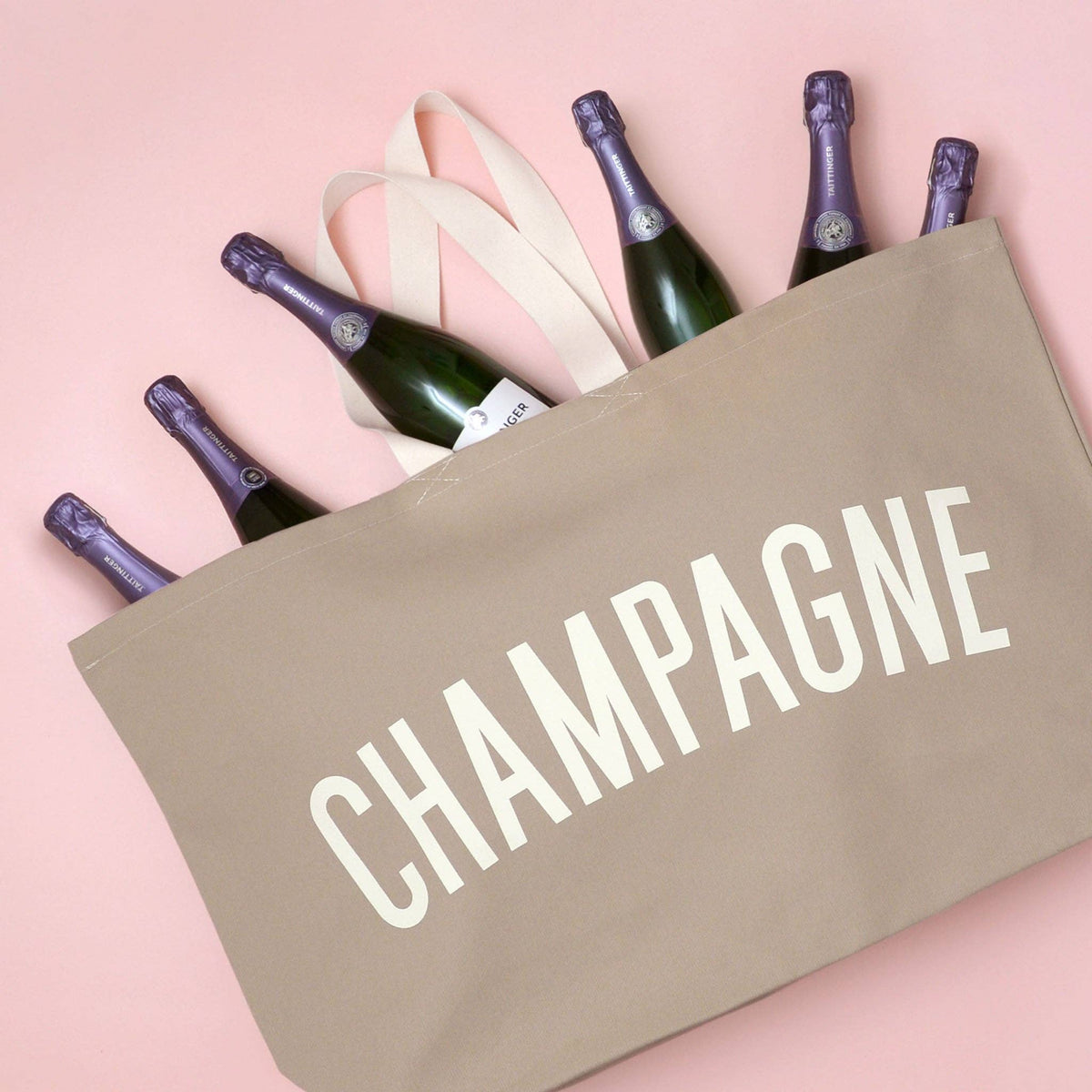 Beige tote bag with 'CHAMPAGNE' text and six bottles of champagne on a pink background