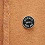 Round black and white enamel pin on a brown textured fabric background