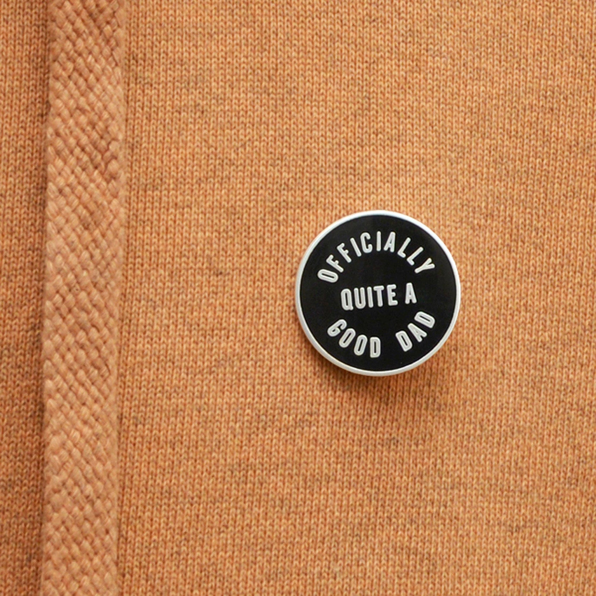 Round black and white enamel pin on a brown textured fabric background