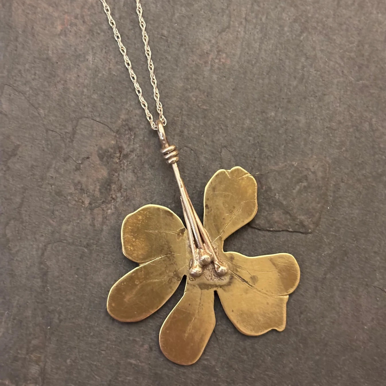 Gold flower-shaped pendant on a chain against a dark textured background