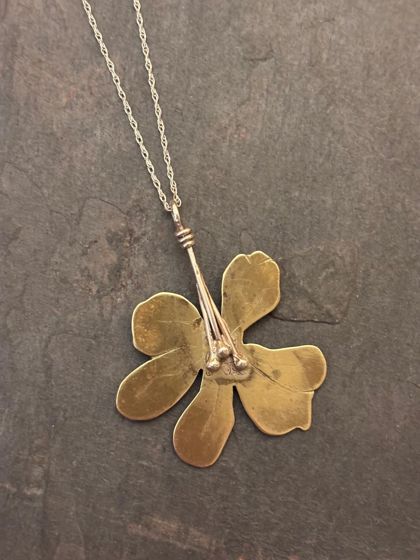Gold flower-shaped pendant on a chain against a dark textured background
