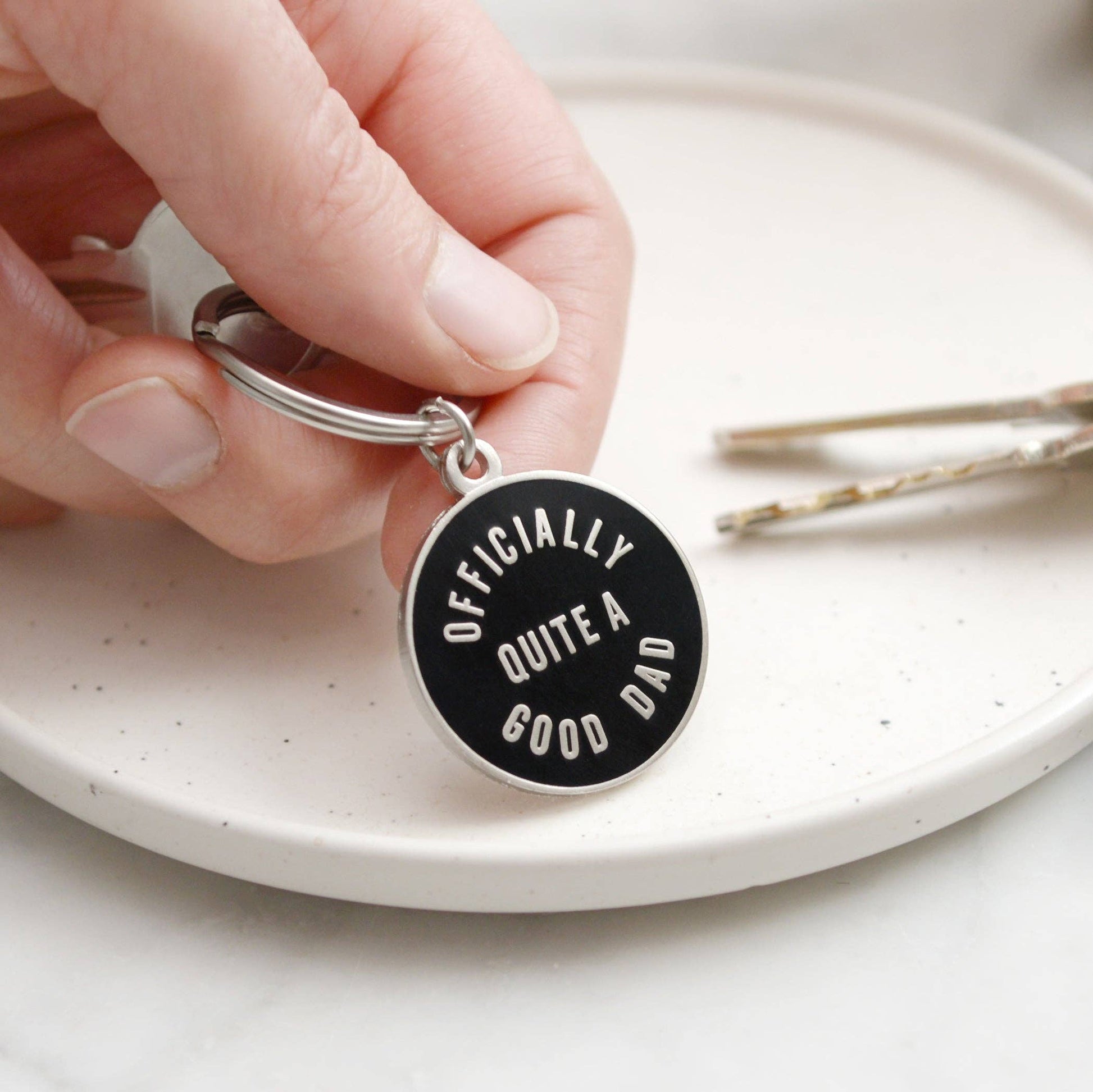 Keychain with 'Officially Quite a Good Dad' text held by a hand on a white plate.