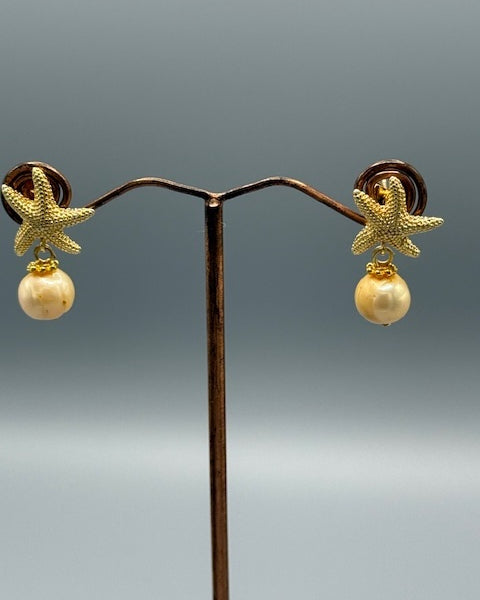Pair of earrings with starfish and pearl design on a gray background