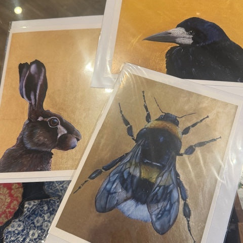 Three artistic prints of a rabbit, raven, and bee on a reflective surface.