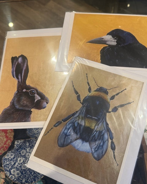 Three artistic prints of a rabbit, raven, and bee on a reflective surface.