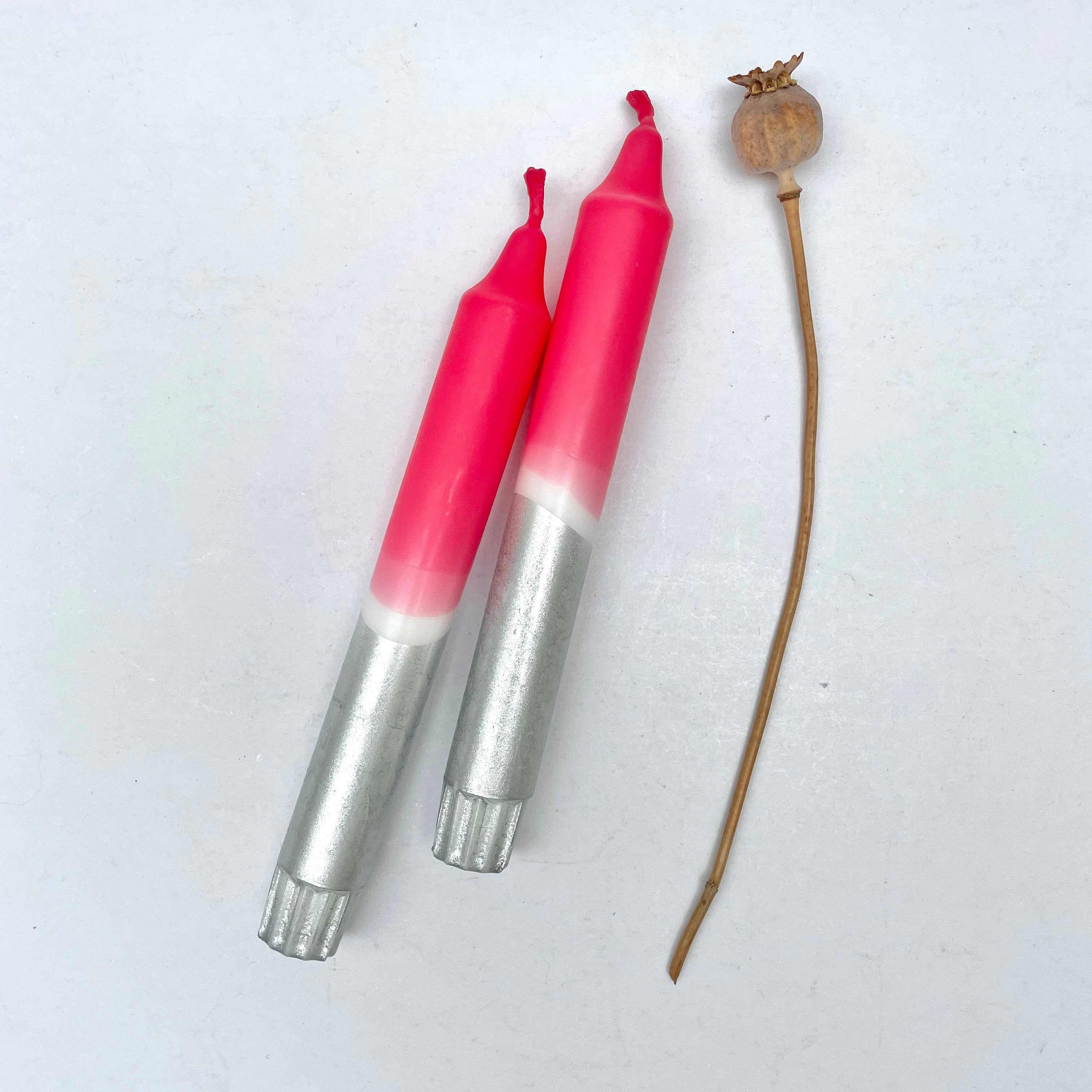 Two pink and silver tools next to a dried plant on a white background