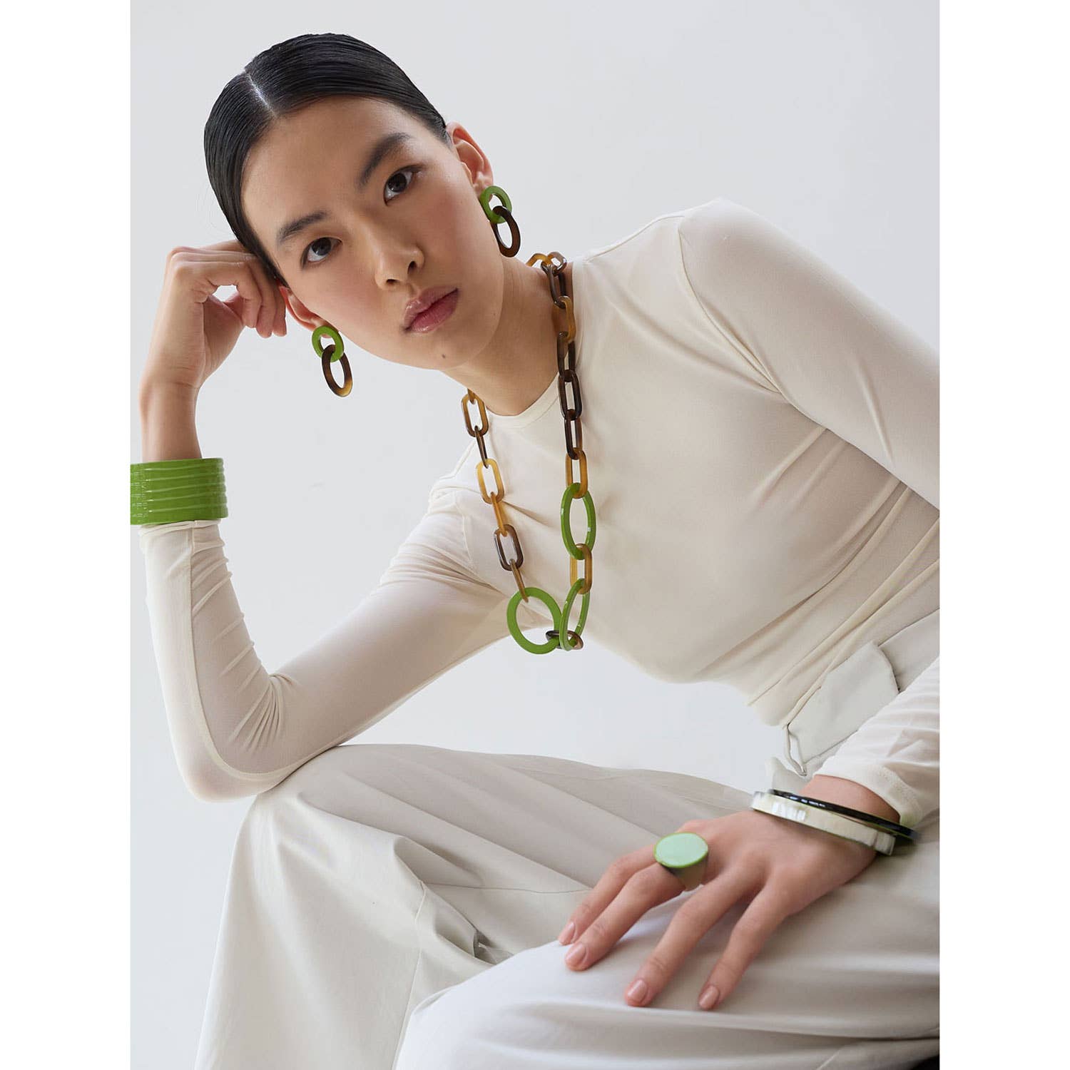 Woman wearing a long necklace with green accents against a white background