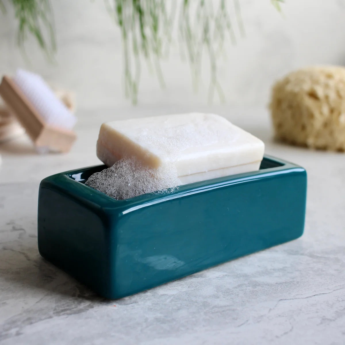 Teal soap dish with a bar of soap and a scrubber on a marble surface.