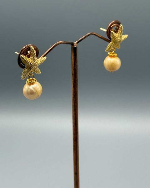 Gold starfish and pearl earrings on a stand against a gray background