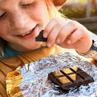 Child holding a chocolate bar over tinfoil with a blurred background