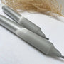 Two gray markers on a white surface with dried plants in the background