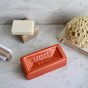 Rectangular terracotta soap dish with 'London' branding on a concrete surface with soap, brush, and sponge.