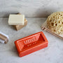 Rectangular terracotta soap dish with 'London' branding on a concrete surface with soap, brush, and sponge.