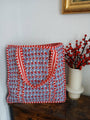 Red and blue patterned bag on a wooden surface with a vase of red berries in the background.