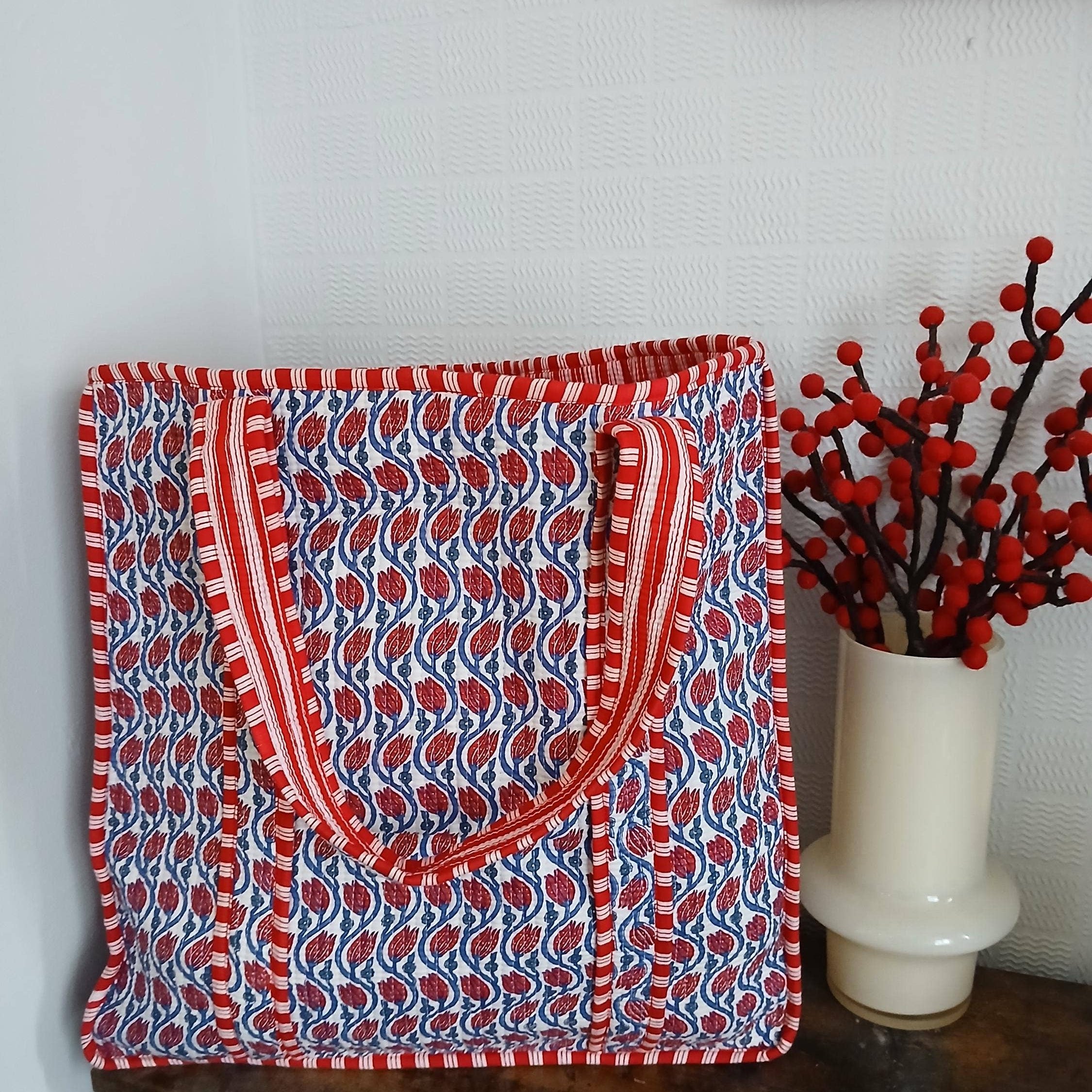 Red and blue patterned bag on a wooden surface with a vase of red berries in the background.