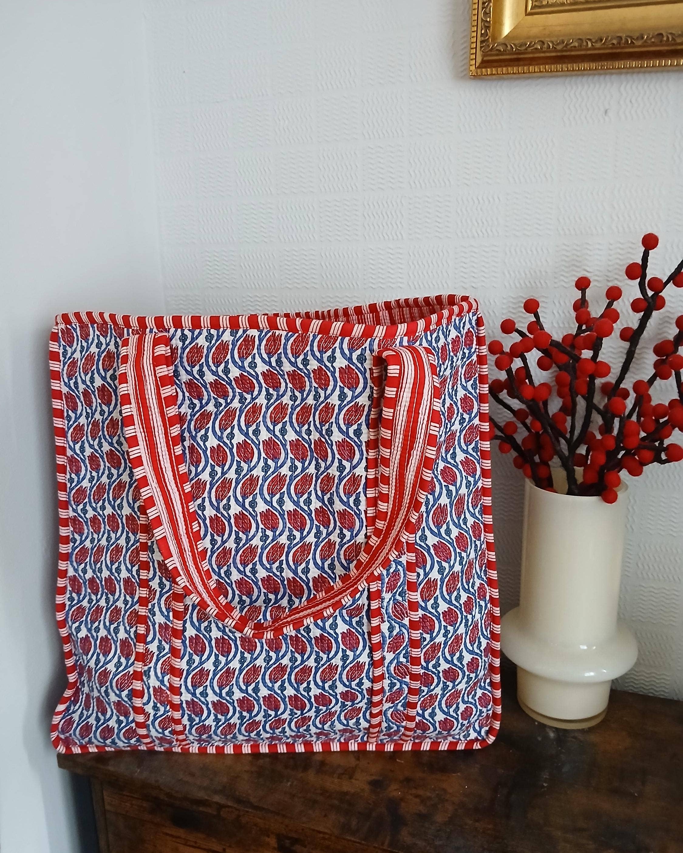 Red and blue patterned bag on a wooden surface with a vase of red berries in the background.
