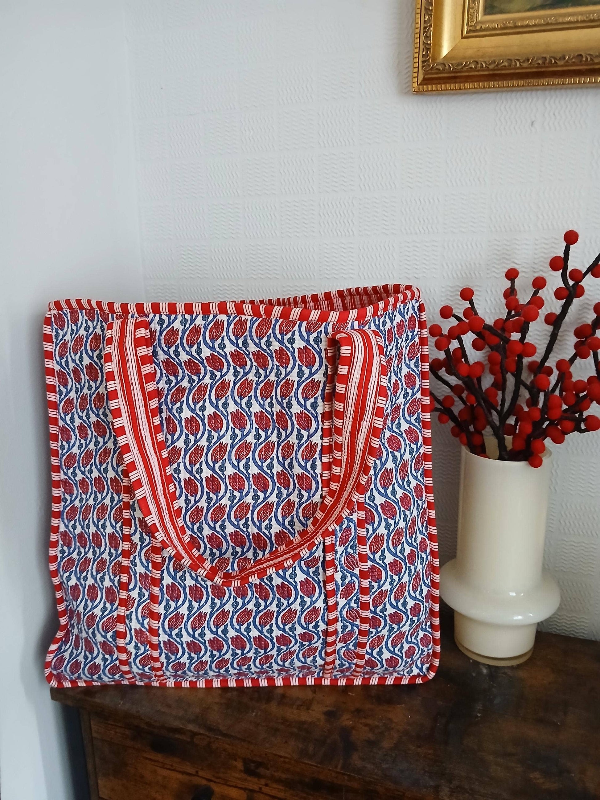 Red and blue patterned bag on a wooden surface with a vase of red berries in the background.